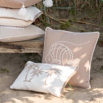 Conjunto de almofadas decorativas bege e branco com bordados e pompons, ao ar livre na areia