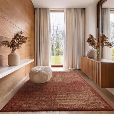 Tapete vermelho retangular em sala com chão de madeira, cortinas brancas, puff branco e vasos com plantas secas