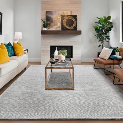 Sala de estar com tapete cinza, sofá creme com almofadas amarelas e verdes, poltronas castanhas, mesa de centro dourada com vidro, lareira e plantas