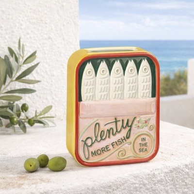 Lata decorativa de cerâmica com design de peixes e texto na frente, em fundo de mar e céu azul.