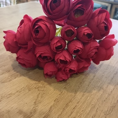 Ramo de flores artificiais vermelhas sobre mesa de madeira clara