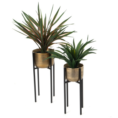 Vasos metálicos dourados com plantas artificiais verdes e suportes pretos altos