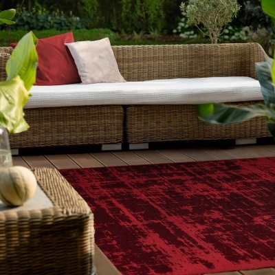 Sofá de rattan com almofadas e tapete vermelho num espaço exterior