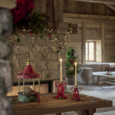 Castiçais vermelhos com velas e caixa decorativa em ferro numa mesa rústica junto a lareira