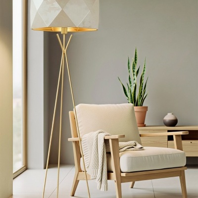 Lâmpada de pé dourada com abajur creme ao lado de poltrona bege com manta tricotada e planta verde em vaso de terracota