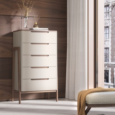 Cômoda alta de cinco gavetas em madeira clara ao lado de janela com cortina branca