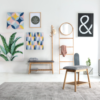 Sala de estar moderna com cadeira, banco, cabideiro de madeira, quadros coloridos e mesa com câmara fotográfica.