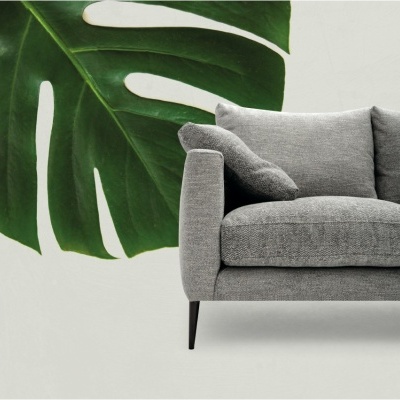 Sofá cinzento com almofadas e parede branca com folha verde.