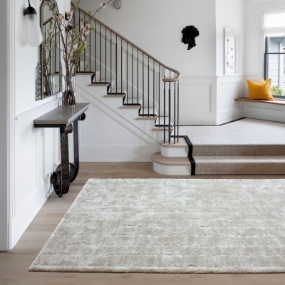 Tapete cinzento claro com padrão geométrico texturizado em sala com escadas e mesa de apoio.