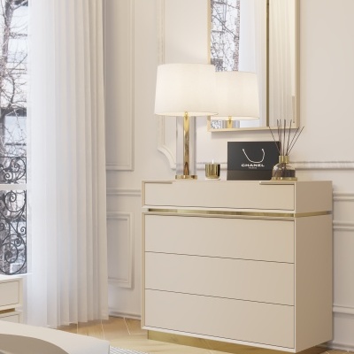 Cômoda bege com detalhes dourados, candeeiro de mesa branco e dourado, espelho, vela, difusor e saco CHANEL numa sala com cortinas brancas.