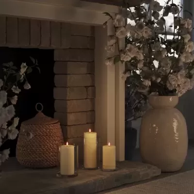 Lareira com velas acesas, cesta de vime e vaso cerâmico com flores brancas