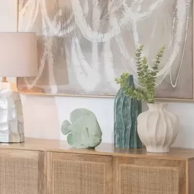 Lâmpada branca com base texturizada e vasos decorativos em cima de cómoda de madeira com pintura abstrata na parede
