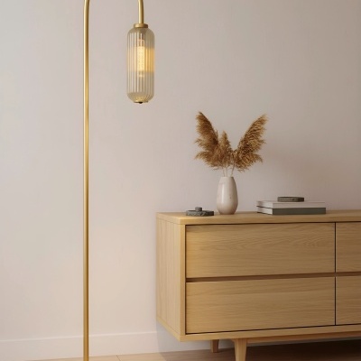 Candeeiro de pé dourado com abajur de vidro ao lado de móvel de madeira claro.