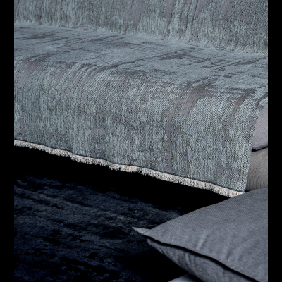 Sofá cinza com tecido texturado e franjas, com almofadas cinzentas empilhadas no chão