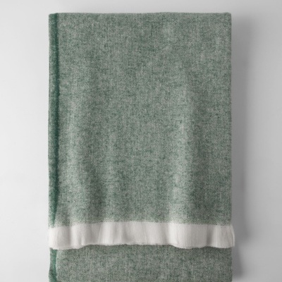 Manta cinza-esverdeada com faixa branca na borda, dobrada sobre superfície branca