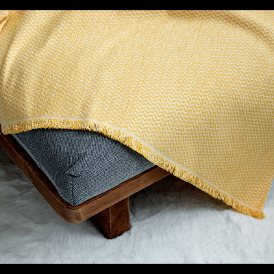 Manta amarela com franjas no sofá cinzento escuro e tapete branco.