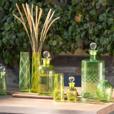Frascos, copos e vasos em vidro verde com padrão gravado numa mesa de madeira