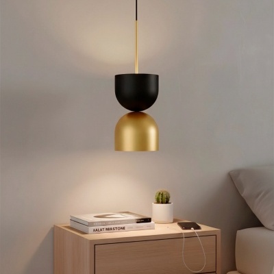 Candeeiro pendente preto e dourado sobre mesa de cabeceira de madeira com cacto, livros e smartphone