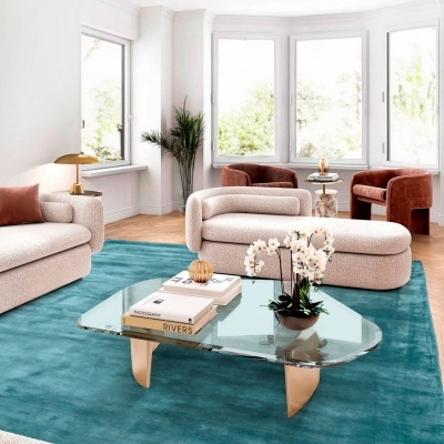 Sala de estar com sofá claro, poltronas castanhas, mesa de vidro e tapete azul.