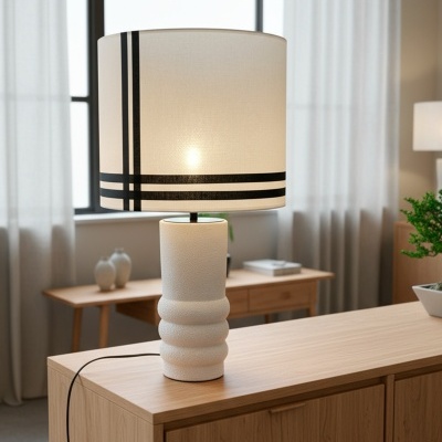 Lâmpada de mesa branca com riscas negras sobre móvel de madeira clara