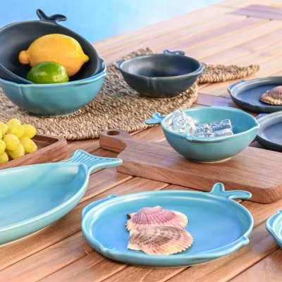 Conjunto de loiça azul em forma de peixe com fruta e conchas decorativas sobre mesa de madeira