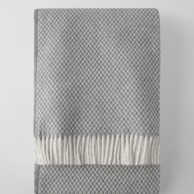 Manta cinzenta com padrão de losangos brancos e franjas brancas.