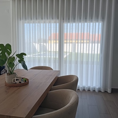 Cortinado branco translúcido em sala moderna com mesa de madeira e cadeiras bege
