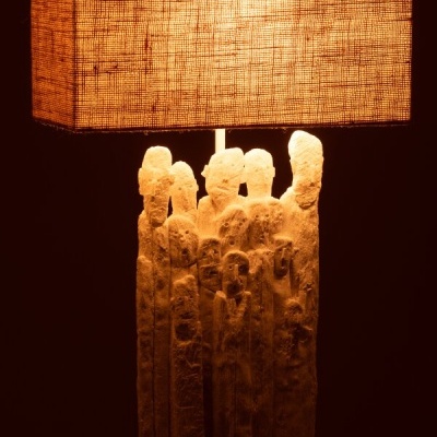 Lâmpada decorativa com base esculpida em forma de figuras humanas e abajur retangular de tecido bege.