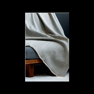 Manta cinzenta com padrão zig-zag sobre sofá azul e base de madeira