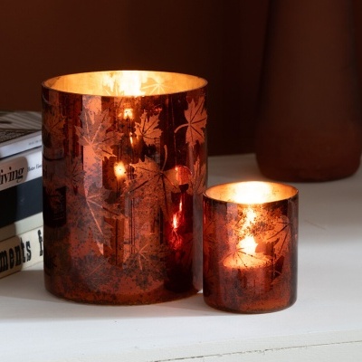 Duas velas acesas em castiçais metálicos decorados com folhas, sobre superfície branca com livros ao lado