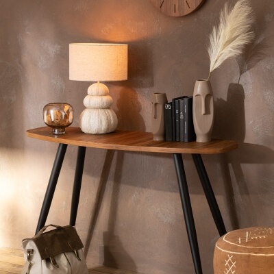 Mesa de madeira com candeeiro, vasos, livros, relógio de parede e mochila num ambiente interior acolhedor