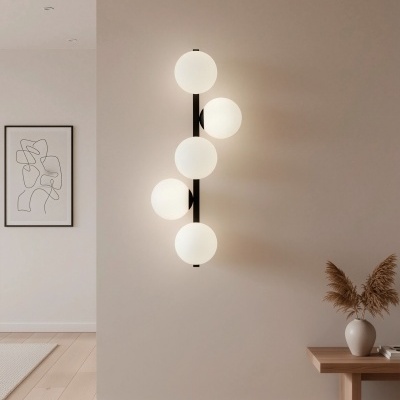 Luminária de parede com cinco globos de vidro branco em parede bege ao lado de móvel com vaso e quadro abstrato.