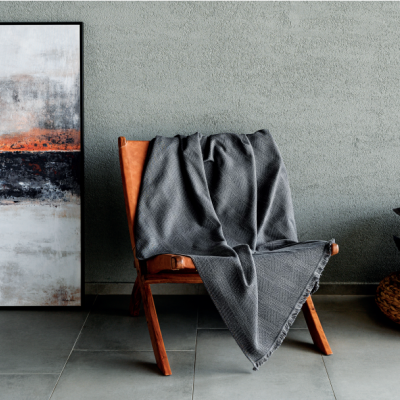 Cadeira de madeira com manta cinza, almofadas e quadro abstrato num ambiente minimalista