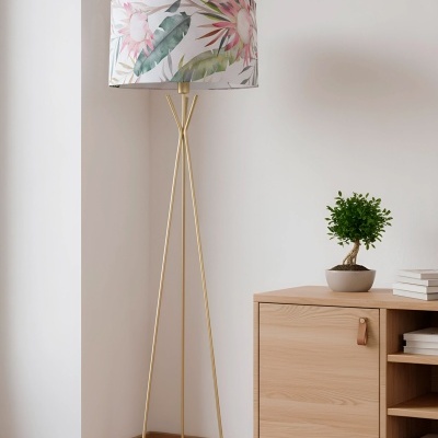Luminária de pé com tripé dourado e cúpula floral ao lado de móvel de madeira clara com planta.
