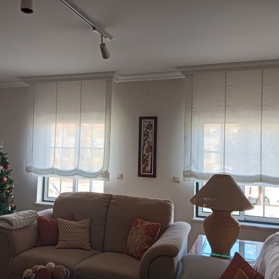 Sala de estar com sofás bege, árvore de Natal e janelas com cortinas brancas