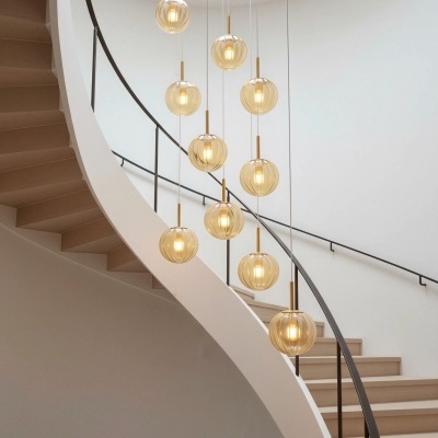 Escada em espiral de madeira clara com candeeiros pendentes redondos dourados