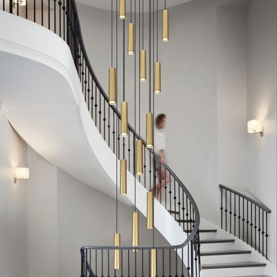 Candeeiro suspenso dourado com múltiplos cilindros pendentes na escadaria curva