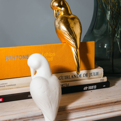 Estatuetas decorativas de pássaros dourado e branco com livros e vaso de vidro