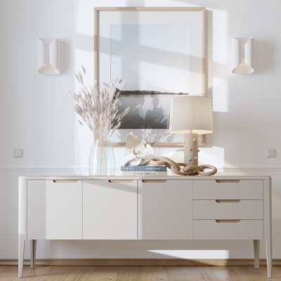 Aparador branco com abajur, vaso e escultura, com quadro na parede e chão de madeira clara