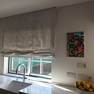 Cozinha com cortina romana cinza, banca branca com cuba dupla e torneira inox, quadro colorido na parede e tigela com limões.