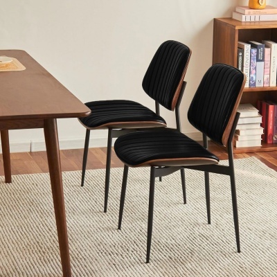 Duas cadeiras pretas com estrutura metálica e detalhes em madeira ao lado de mesa e estante de madeira em ambiente interior.