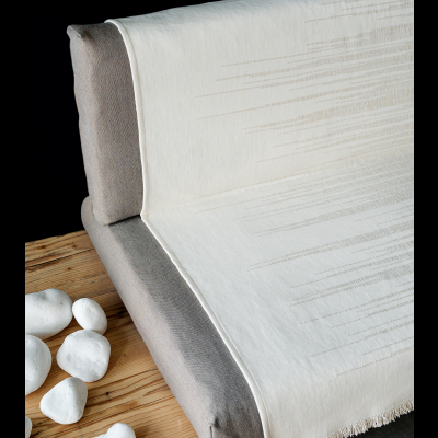 Manta branca com linhas bege em sofá cinza ao lado de mesa de madeira com pedras brancas.