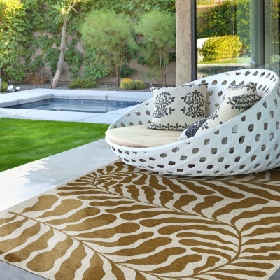 Cadeira de exterior redonda branca, almofadas decorativas e tapete bege com padrão de folha