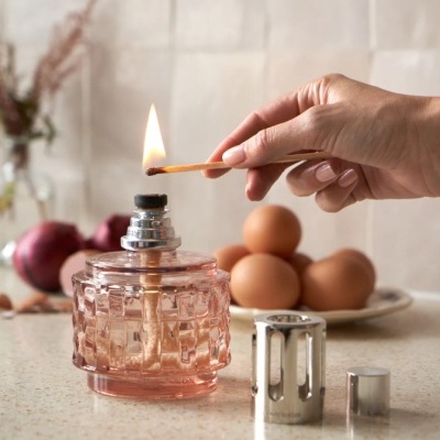 Frasco de vidro rosa para combustivel de lampada com tampa metálica e ovos ao fundo