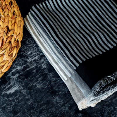 Manta dobrada com riscas brancas e pretas e franjas ao lado de objeto trançado de palha sobre superfície escura