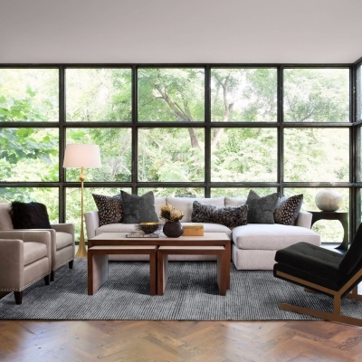 Sala de estar moderna com sofá branco, poltronas bege, cadeira preta, mesa de centro de madeira e piso em madeira