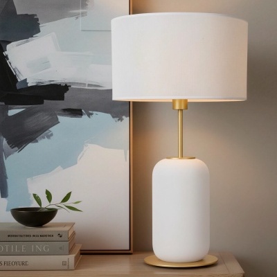 Abajur branco com detalhes dourados sobre móvel de madeira com decoração e quadro abstrato.