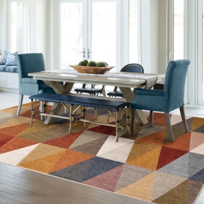 mesa de jantar de madeira clara com cadeiras e banco azuis sobre tapete geométrico colorido