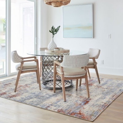 Mesa de jantar redonda de vidro com cadeiras de madeira e ráfia branca sobre tapete colorido