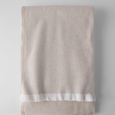 Manta bege claro dobrada com borda branca frisada